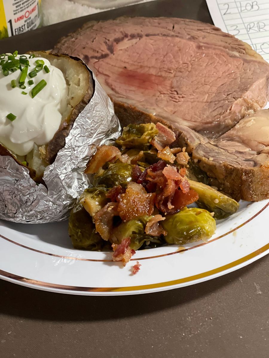 Sliced prime rib plated with a loaded baked potato and bacon Brussels sprouts