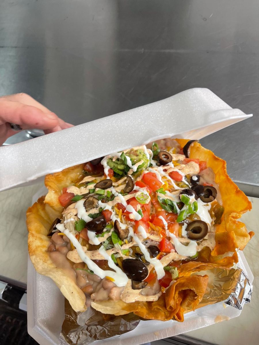 Stuffed sopapilla smothered with crema, olives and tomatoes in a to-go box