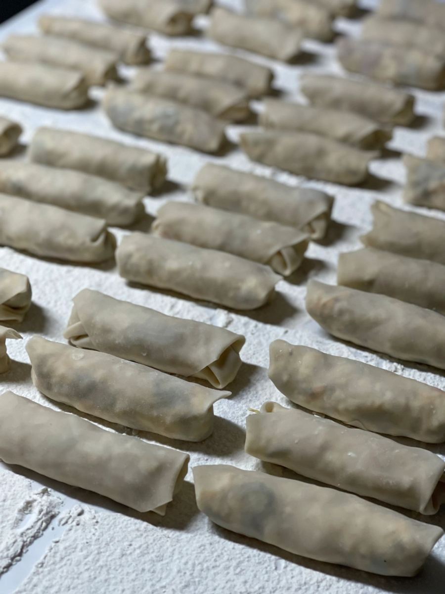 Rows of taquitos being hand-rolled on a floured counter