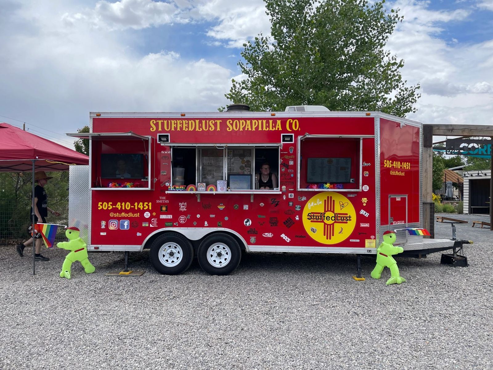 The bright red Stuffed Lust trailer covered in band stickers and pride flags, with the owner smiling in the service window